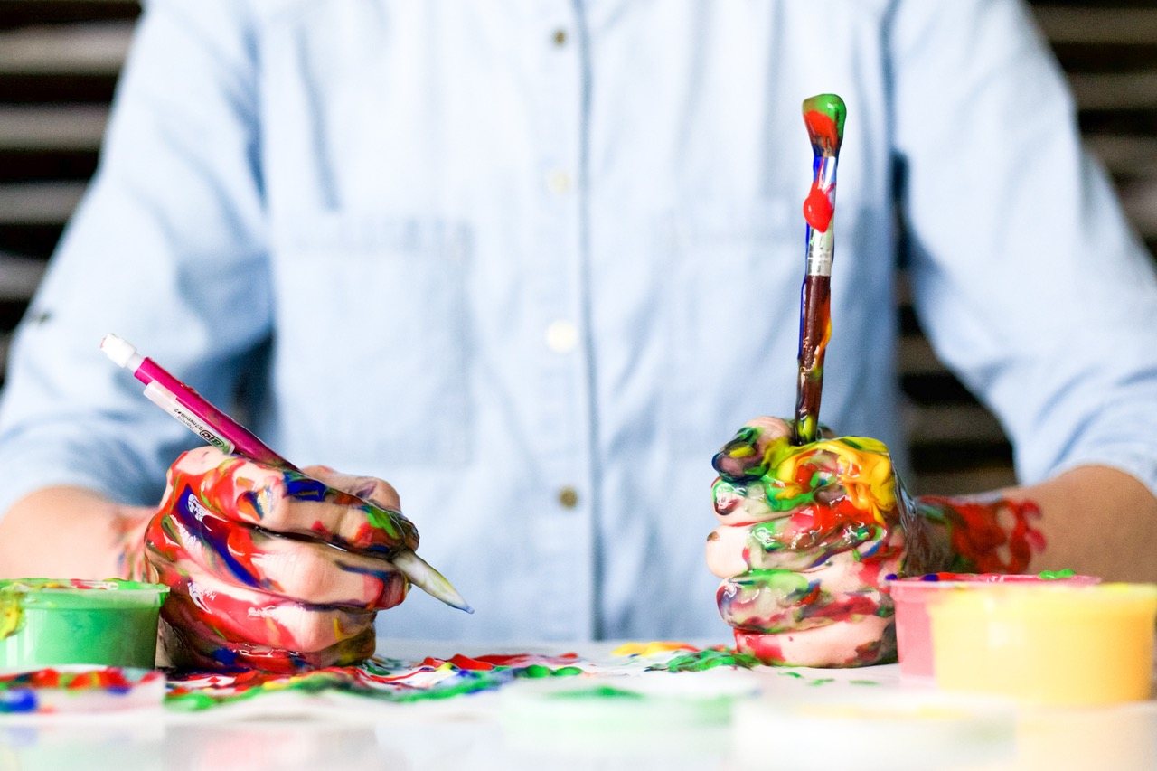 Mains couvertes de peinture tenant un pinceau et un crayon